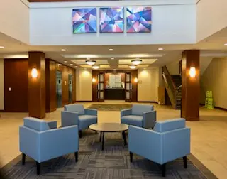 An image of a waiting room, with four blue chairs facing inward to a small coffee table.